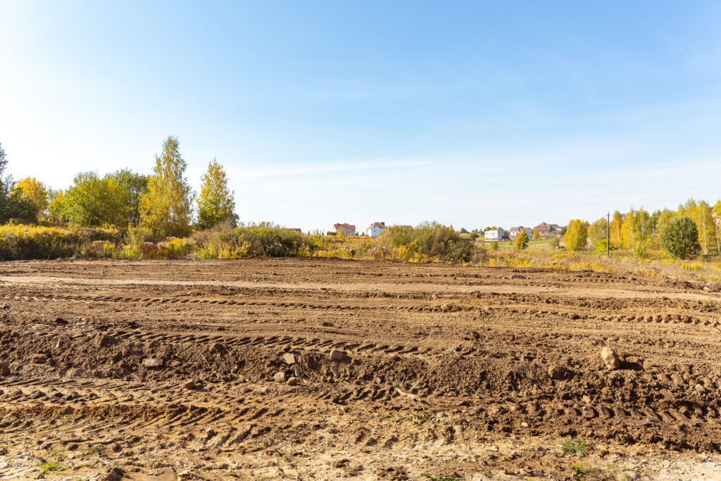 Empty land plot with tire prints prepared for new housing in rural area. Clearing and leveling of construction site. Earthworks for landscape design. Land reclamation for private property development.